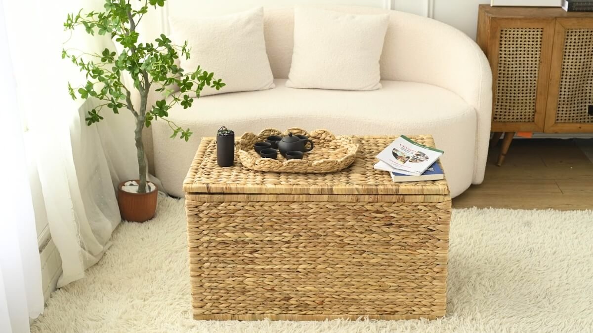 Wicker storage trunk used as a coffee table, styled with books, tea set, and indoor plant in a cozy living room.