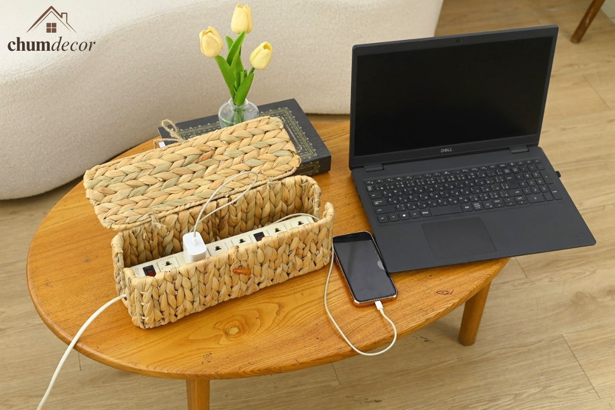 Wicker cable management box with lid open, placed on a wooden table beside a laptop, showcasing stylish and breathable cord storage by ChumDecor.