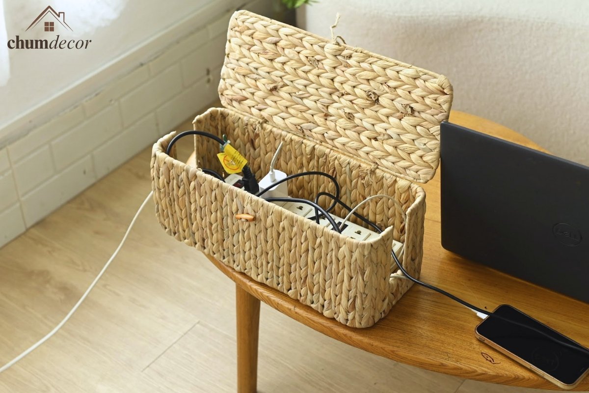 Open wicker cable management boxes showing power strip and charging cables neatly hidden on a wooden table in a bright home office.