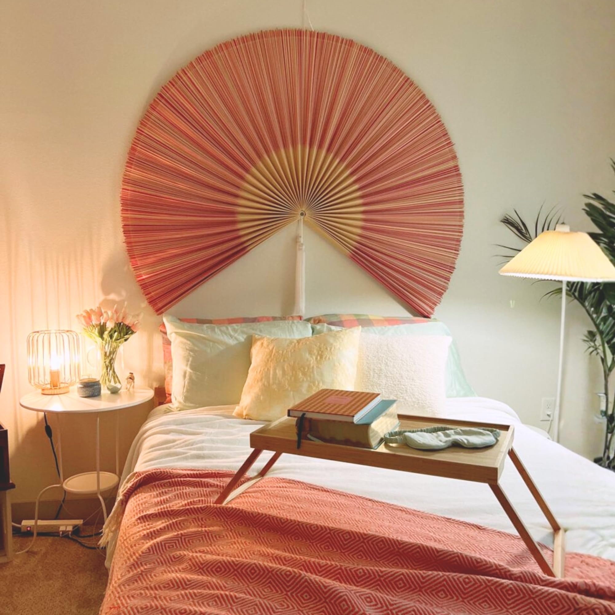 Handmade pink wall fan crafted from natural bamboo displayed as elegant wall decor above a bed in a cozy bedroom
